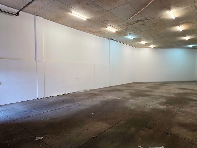 Spacious industrial utility area featuring an exposed concrete ceiling, fluorescent lighting, and durable concrete flooring, suitable for storage or workshop use.