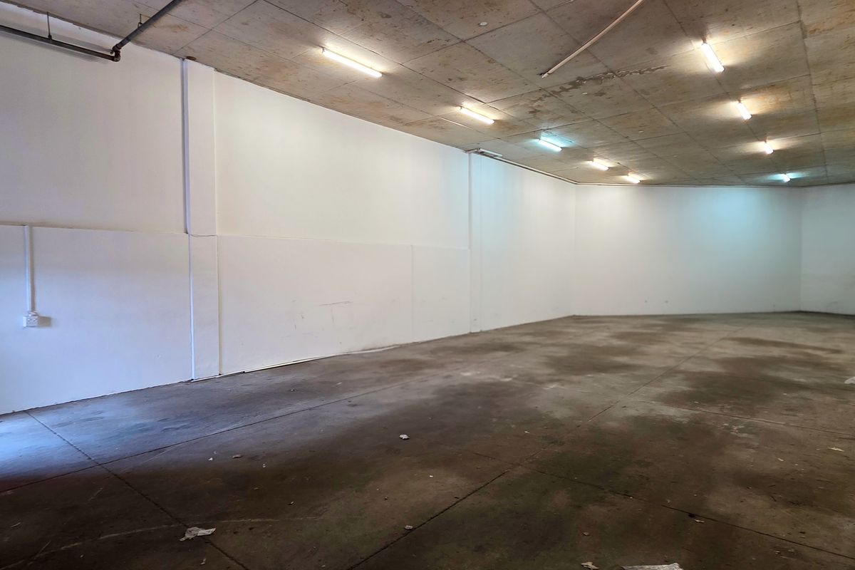 Spacious industrial utility area featuring an exposed concrete ceiling, fluorescent lighting, and durable concrete flooring, suitable for storage or workshop use.