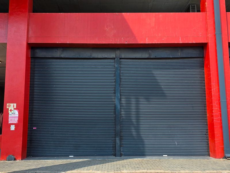Industrial property frontage featuring secure roller shutter doors, red structural steel beams, and a paved driveway area.