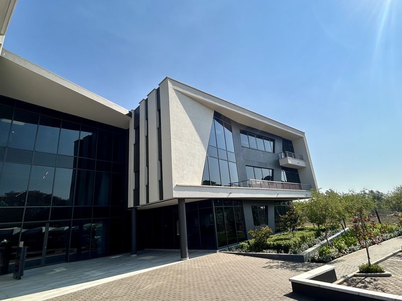 Modern multi-story office building featuring a striking glass facade, paved driveway, and integrated balconies with contemporary architectural design.