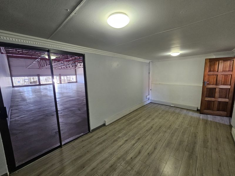 An empty office space featuring laminate flooring, crown molding, and a sliding glass door providing a view into a larger open-plan retail area.