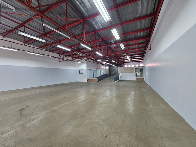 Spacious open-plan retail or industrial warehouse area featuring high exposed red steel trusses, concrete flooring, and a convenient internal ramp for access.