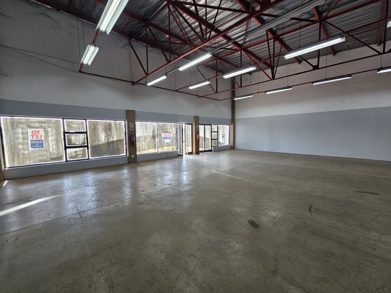 Spacious open-plan retail unit featuring high exposed steel roof trusses, polished concrete flooring, and large street-facing display windows for maximum visibility.