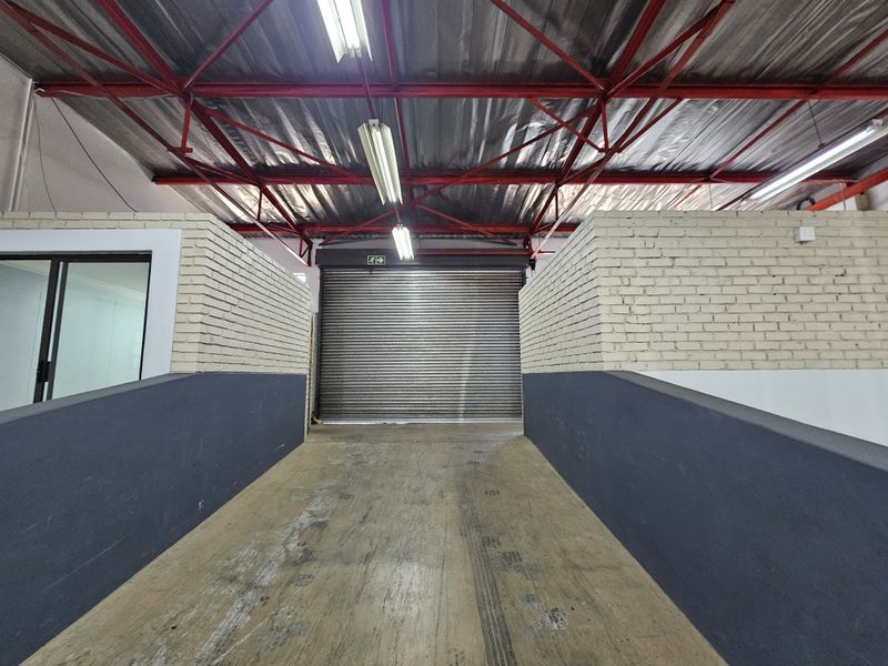 A functional utility or loading area featuring a secure roller shutter door, exposed steel roof trusses, and concrete ramp access.