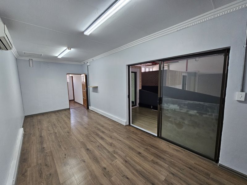 A bright, empty office space featuring laminate wood flooring, crown molding, fluorescent lighting, and a sliding glass door leading to an adjacent area.