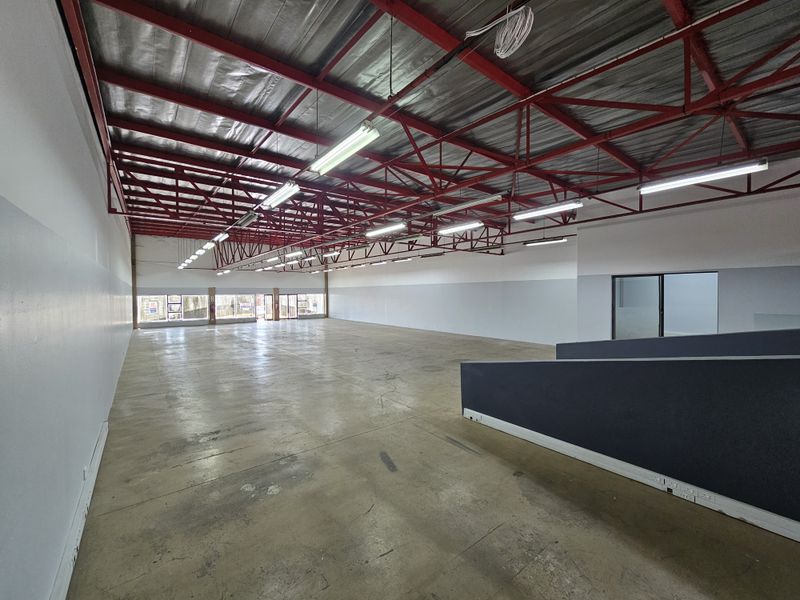 Spacious open-plan retail unit featuring high exposed red steel roof trusses, polished concrete flooring, and ample natural light through large storefront windows.