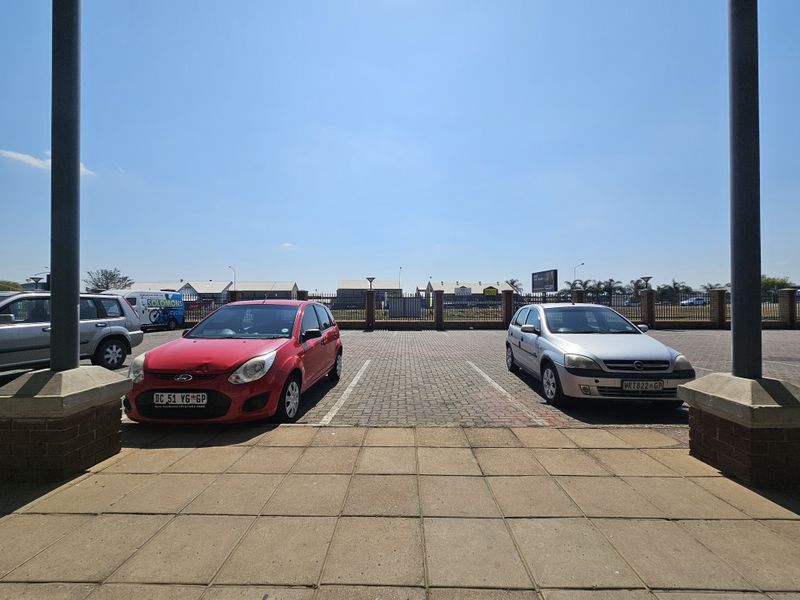 A paved outdoor parking area featuring brick perimeter walls and metal fencing, viewed from a covered entrance area.