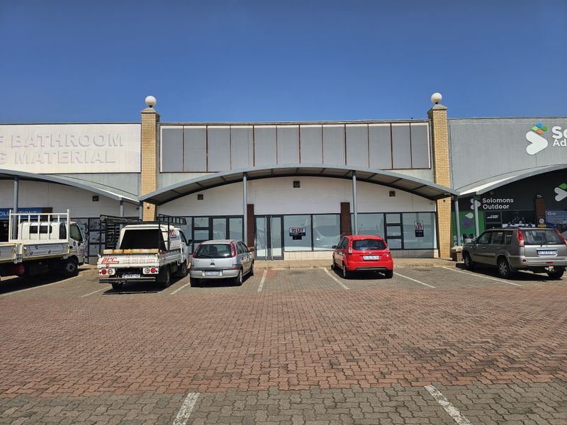 Front elevation of a retail unit featuring a paved parking area, aluminium storefront, and a curved metal awning.
