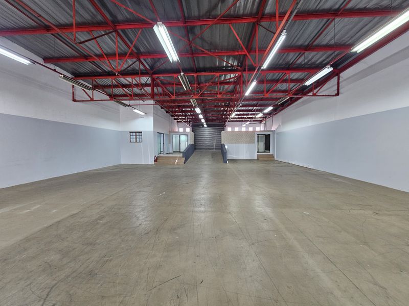 Spacious open-plan retail or warehouse space featuring high exposed red steel roof trusses, concrete flooring, and a convenient internal loading ramp.