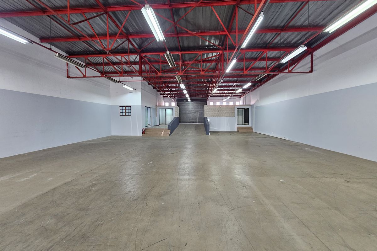 Spacious open-plan retail or warehouse space featuring high exposed red steel roof trusses, concrete flooring, and a convenient internal loading ramp.