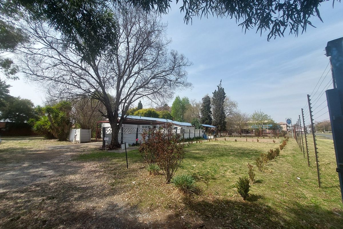 Spacious rear garden area featuring established trees, lawn, and secure perimeter electric fencing with a covered outdoor structure.