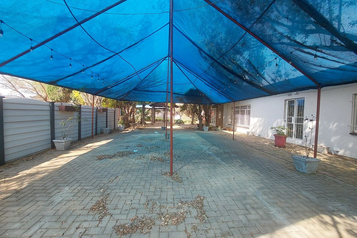 Outdoor paved patio area featuring a large blue shade cloth canopy supported by metal poles, providing a covered space for restaurant seating.