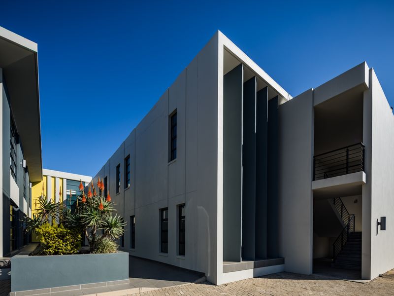 Modern office building exterior featuring clean architectural lines, vertical metal louvers, a paved courtyard area, and an external staircase.