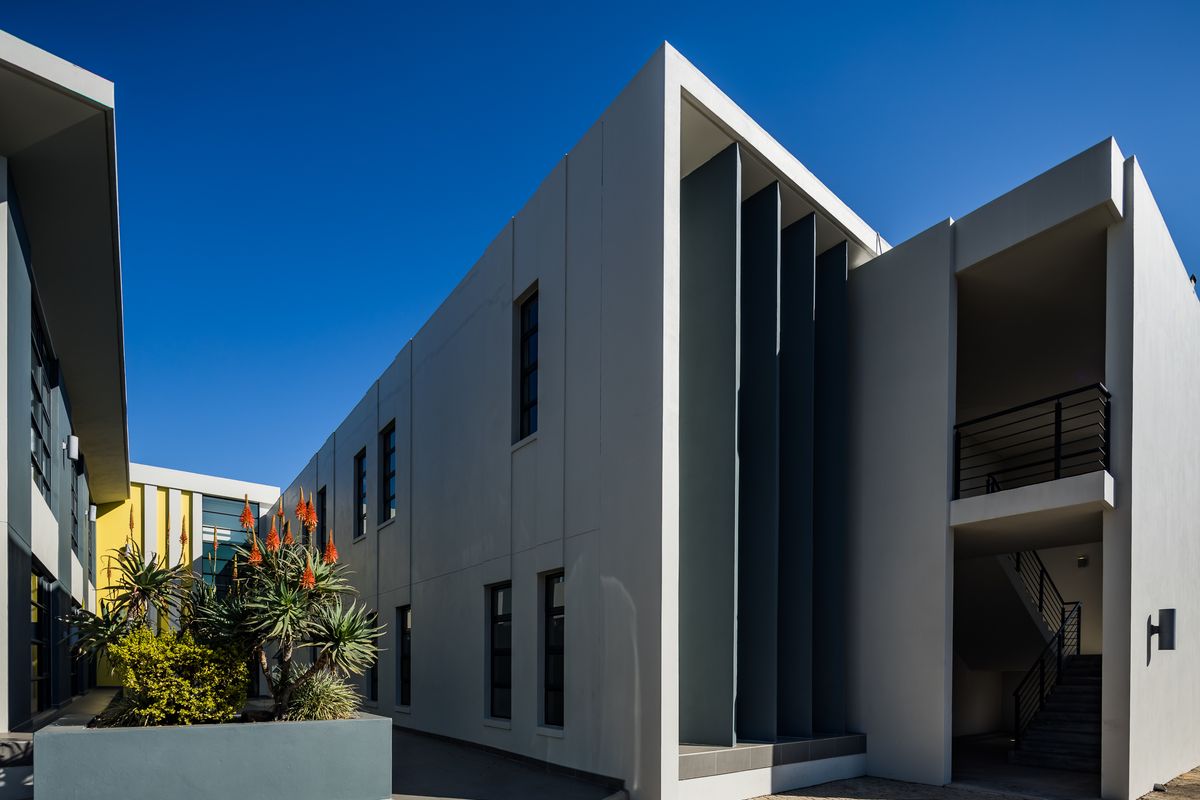 Modern office building exterior featuring clean architectural lines, vertical metal louvers, a paved courtyard area, and an external staircase.