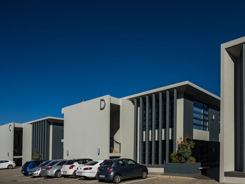 A modern office park complex featuring contemporary architectural design with vertical fins, large glass windows, and dedicated paved parking spaces.