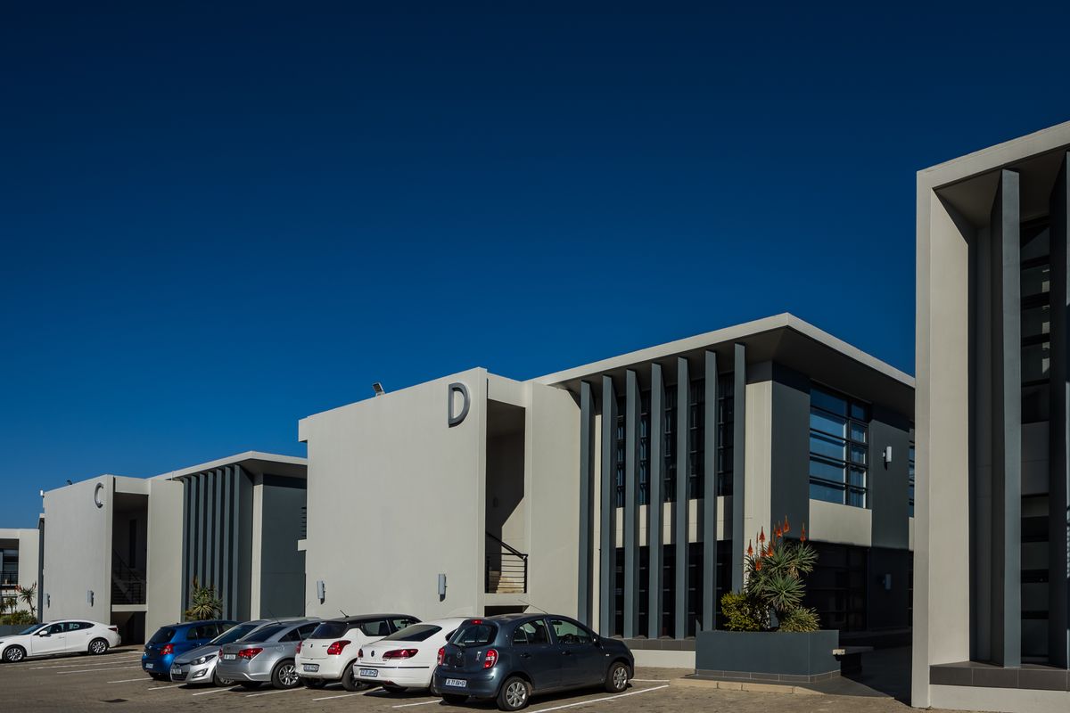A modern office park complex featuring contemporary architectural design with vertical fins, large glass windows, and dedicated paved parking spaces.