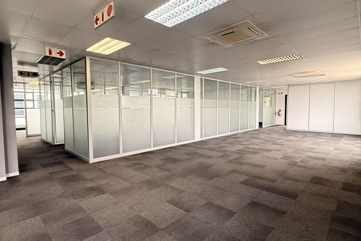 Spacious open-plan office area featuring glass partitioned meeting rooms, suspended ceilings with recessed lighting, and durable carpet tiles throughout.