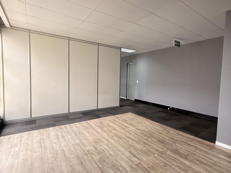 A bright, vacant office space featuring a mix of wood-look vinyl and carpet flooring, suspended ceilings, and modern partition walls.
