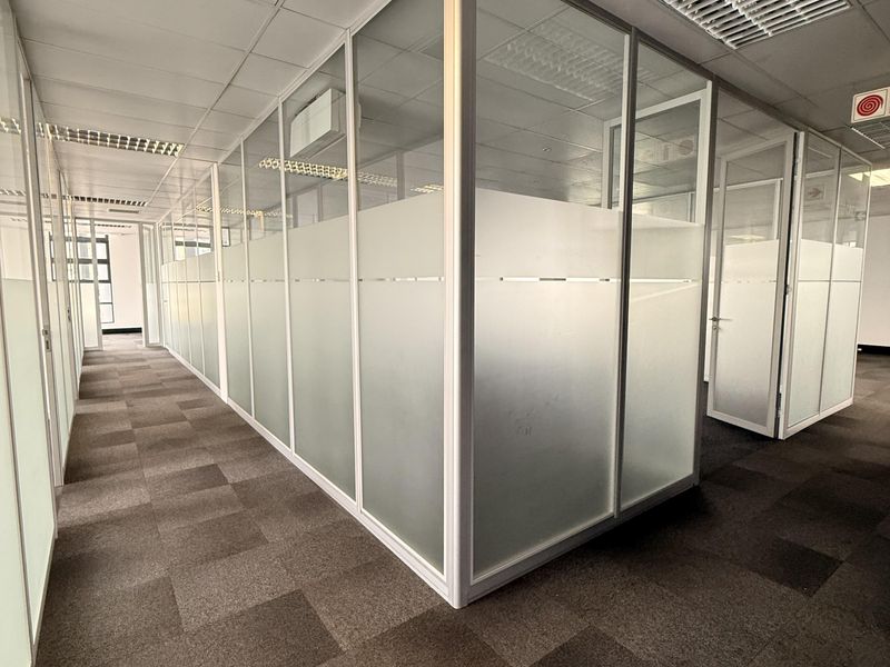Modern office space featuring glass partition walls, suspended ceilings with integrated lighting, air conditioning vents, and professional carpet tile flooring.