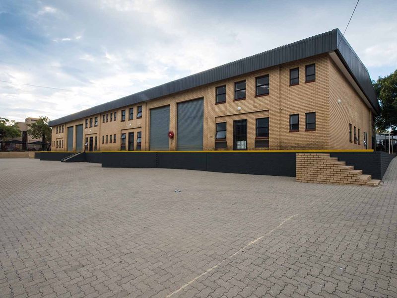 Industrial warehouse facility featuring a large paved yard, multiple roller shutter doors, and a raised loading dock area.