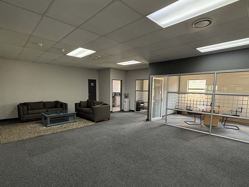 Spacious open-plan office area featuring a glass-partitioned meeting room, suspended ceiling with recessed lighting, and professional carpeted flooring.