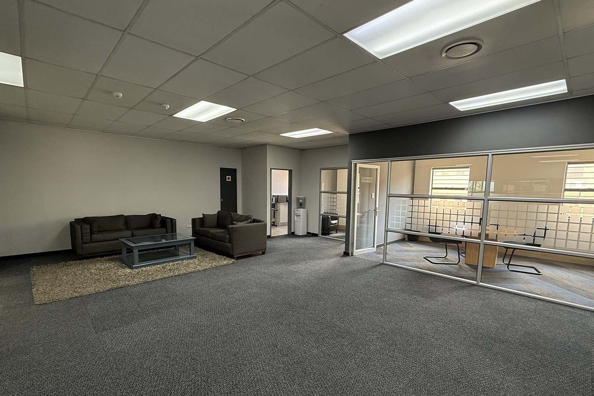 Spacious open-plan office area featuring a glass-partitioned meeting room, suspended ceiling with recessed lighting, and professional carpeted flooring.
