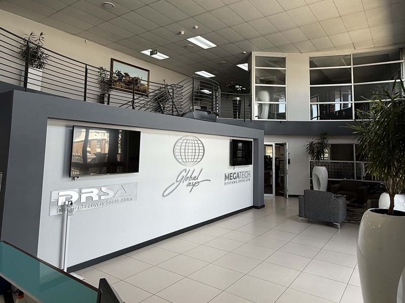 Spacious industrial reception area featuring a mezzanine level, modern tiled flooring, and professional glass partitioning with integrated corporate branding.