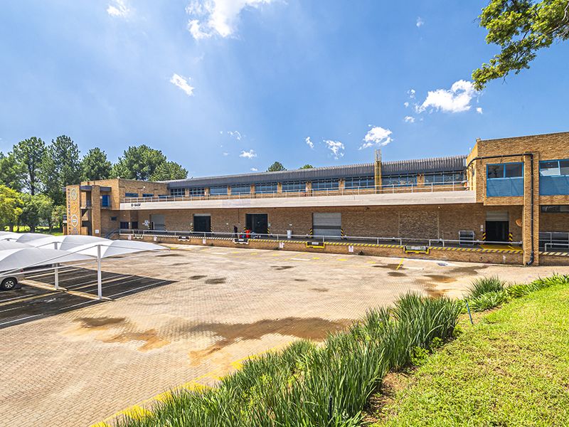 Rear view of a commercial office and warehouse facility featuring multiple loading bays, roller shutter doors, paved yard area, and covered parking structures.