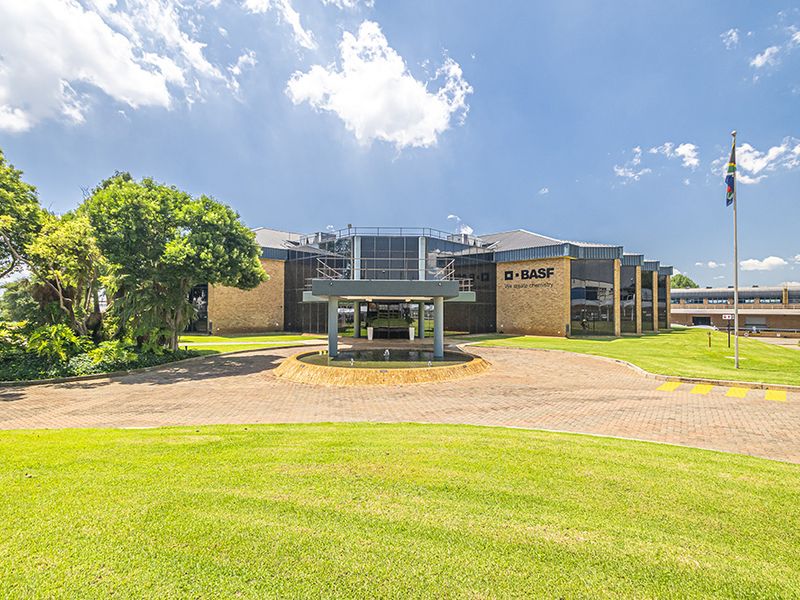 A professional exterior view of the office building featuring a paved driveway, manicured lawns, and a prominent glass-fronted entrance portico.