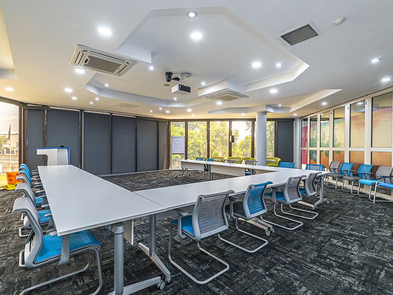 A professional boardroom or meeting space featuring U-shaped table configuration, recessed ceiling lighting, ducted air conditioning, and expansive windows providing natural light.