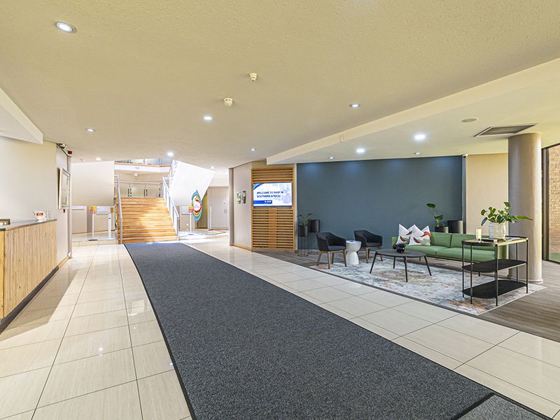 A modern, well-lit office reception area featuring a reception desk, tiled flooring, and a staircase leading to the upper level.
