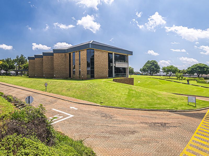 A professional exterior view of a modern brick office building featuring large glass windows, a paved driveway, and well-maintained landscaped grounds.