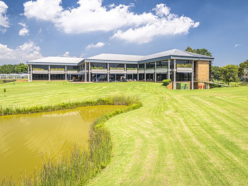 A professional exterior view of a modern office building featuring a large landscaped lawn, a pond, and extensive glass facade elements.