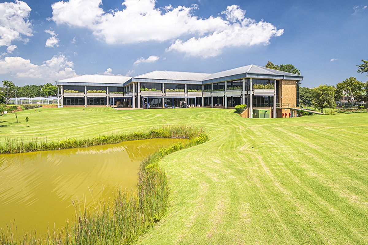 A professional exterior view of a modern office building featuring a large landscaped lawn, a pond, and extensive glass facade elements.