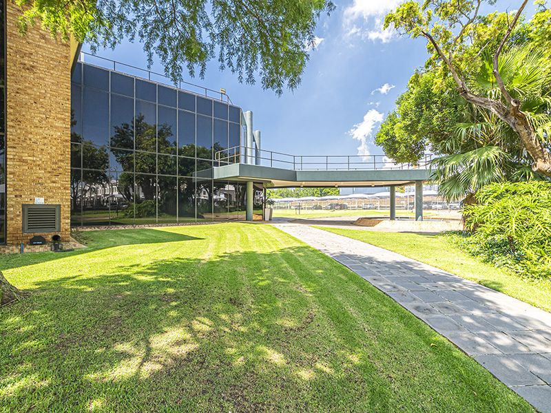 A well-maintained office exterior featuring a modern glass curtain wall, brick facade, and an elevated pedestrian walkway set within landscaped grounds.