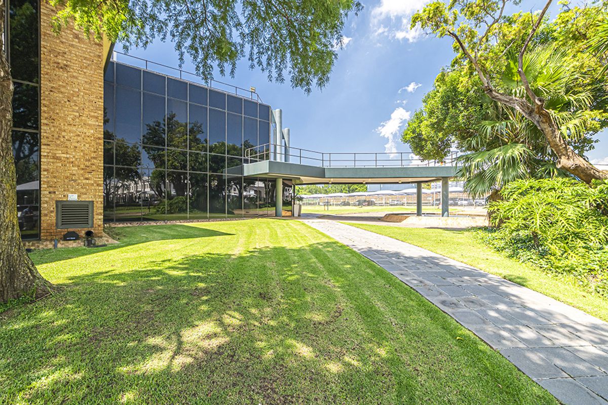 A well-maintained office exterior featuring a modern glass curtain wall, brick facade, and an elevated pedestrian walkway set within landscaped grounds.