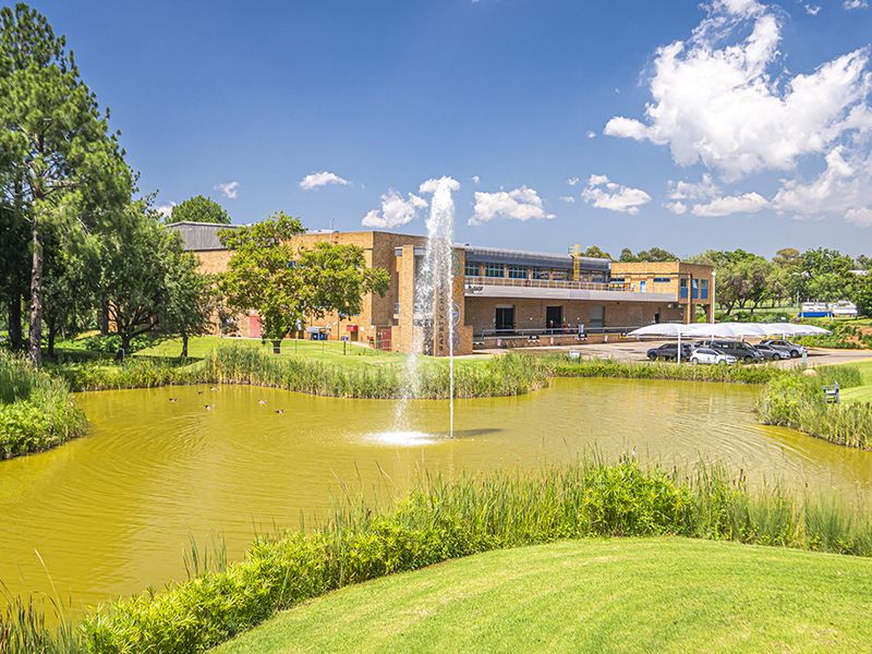 A scenic view of the office property featuring a landscaped pond with a fountain, manicured grounds, and a covered parking area.