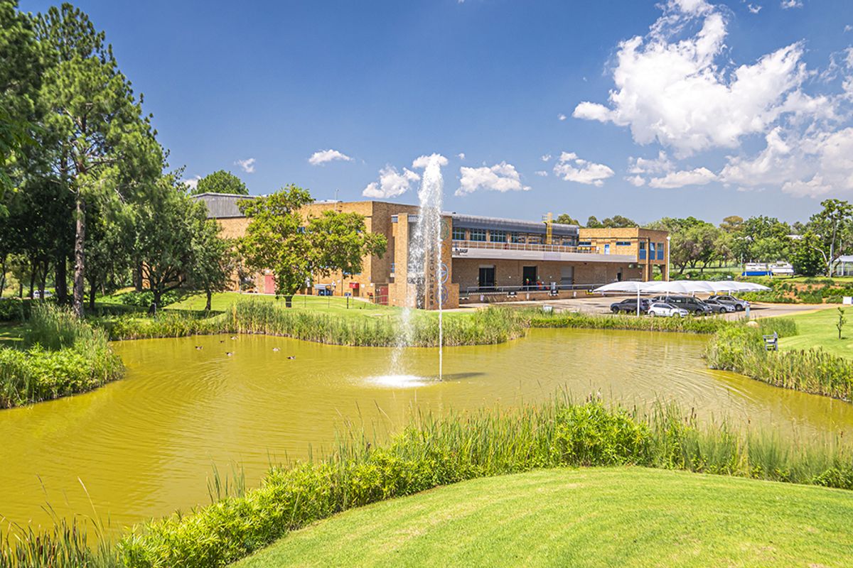 A scenic view of the office property featuring a landscaped pond with a fountain, manicured grounds, and a covered parking area.