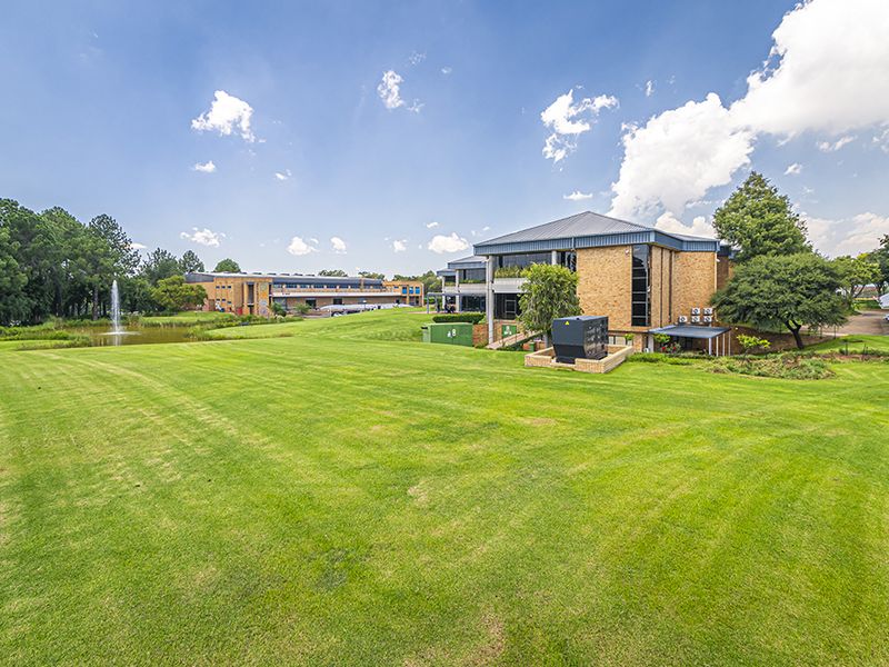 A wide-angle view of the office property exterior, featuring expansive manicured lawns, a decorative water fountain, and well-maintained brick building facades.
