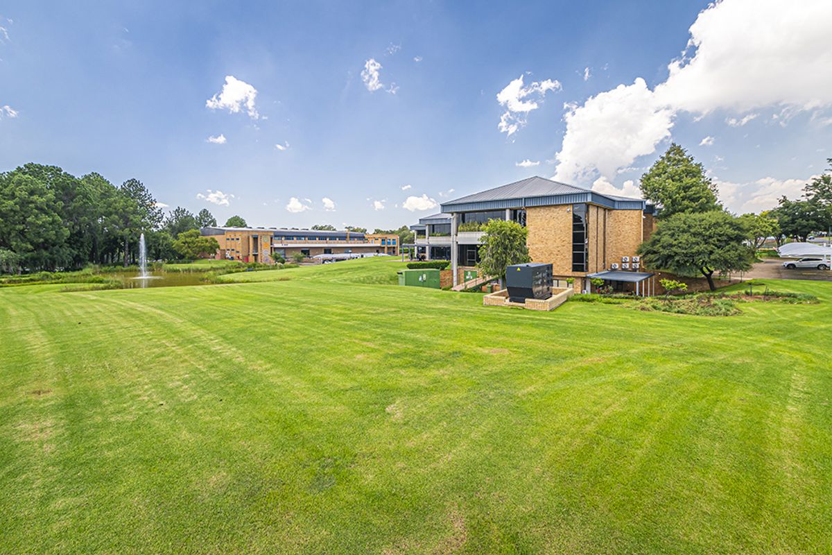 A wide-angle view of the office property exterior, featuring expansive manicured lawns, a decorative water fountain, and well-maintained brick building facades.