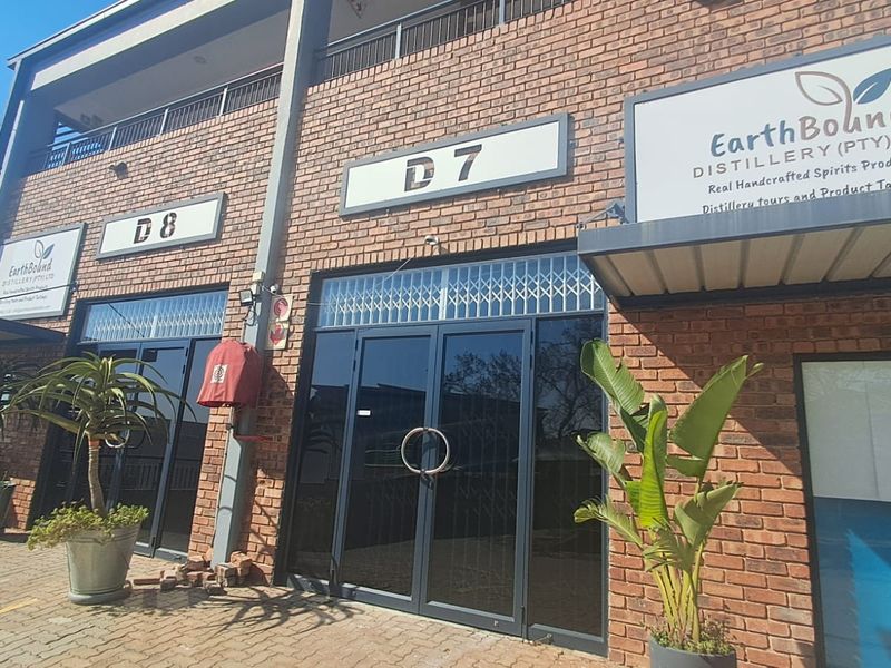 Front exterior view of an industrial unit featuring brick facade, glass double doors with security gates, and prominent business signage.