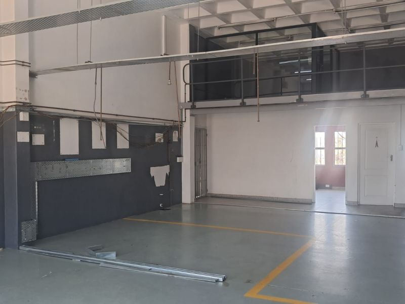Industrial utility space featuring a mezzanine level, exposed ceiling structure, epoxy flooring, and an integrated office area with a private toilet.