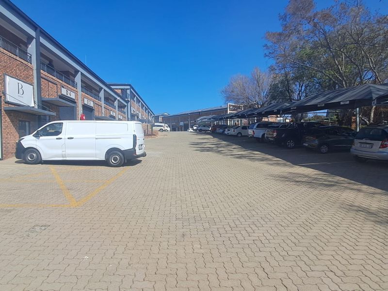 Exterior view of an industrial office park featuring a paved driveway, covered parking bays, and brick-faced building units.