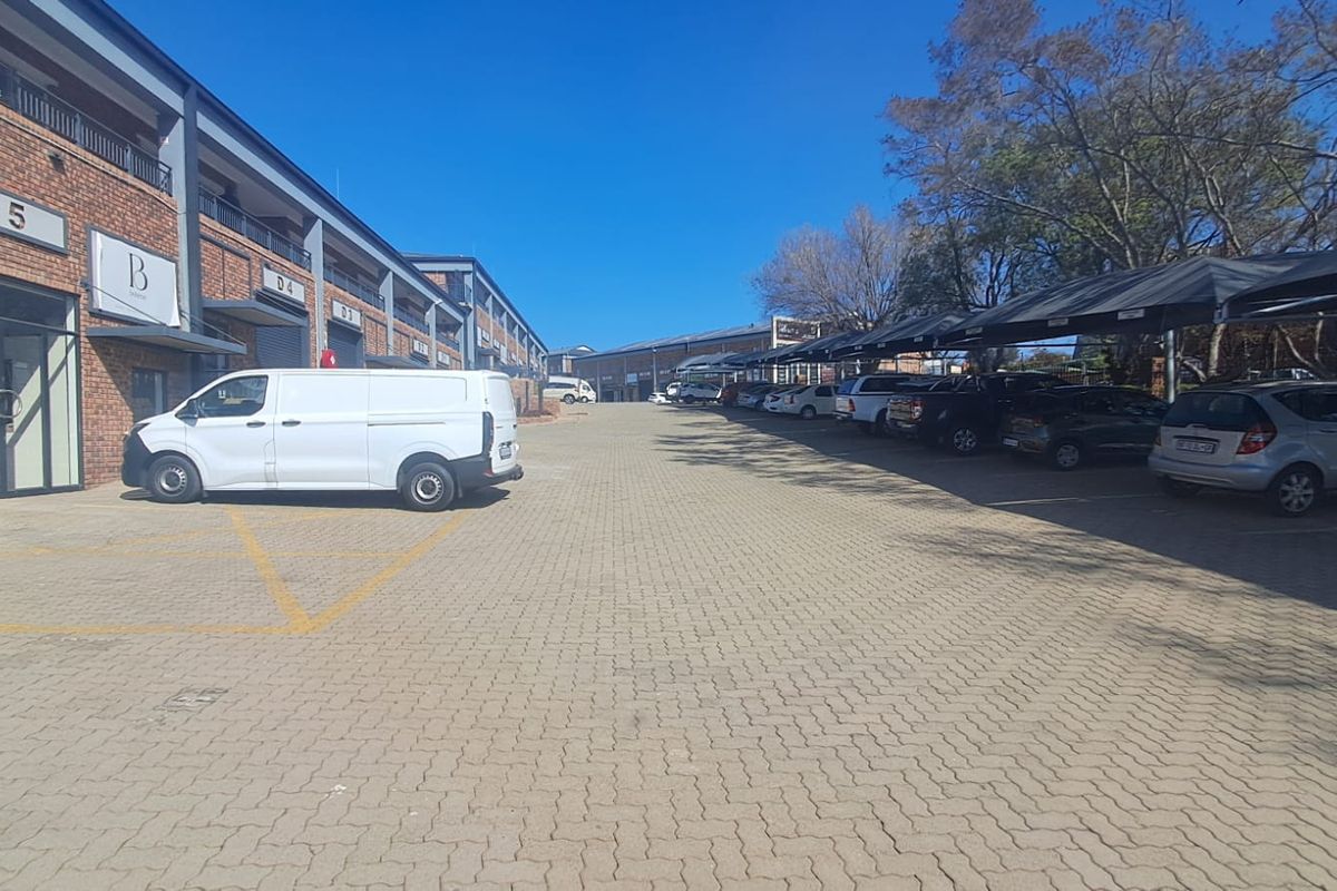 Exterior view of an industrial office park featuring a paved driveway, covered parking bays, and brick-faced building units.