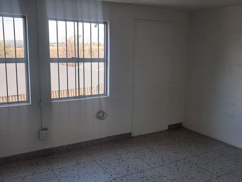 An empty office space featuring terrazzo flooring, security bars on the windows, and basic wall finishes, suitable for a functional workspace.