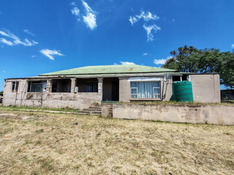 Front elevation of a farm house showing significant wear to the exterior plaster and roof, featuring a concrete retaining wall and water tank.