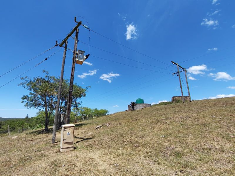 Open farm land featuring utility infrastructure, including electrical poles with a transformer and a water storage tank on a concrete base.