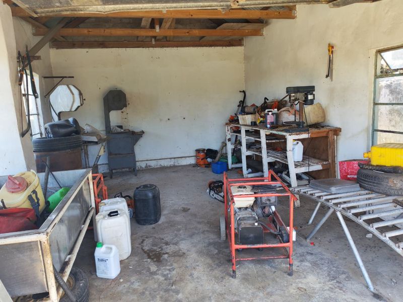 A rustic utility or workshop space featuring exposed timber roof trusses, concrete flooring, and built-in workbench, suitable for farm maintenance or storage.