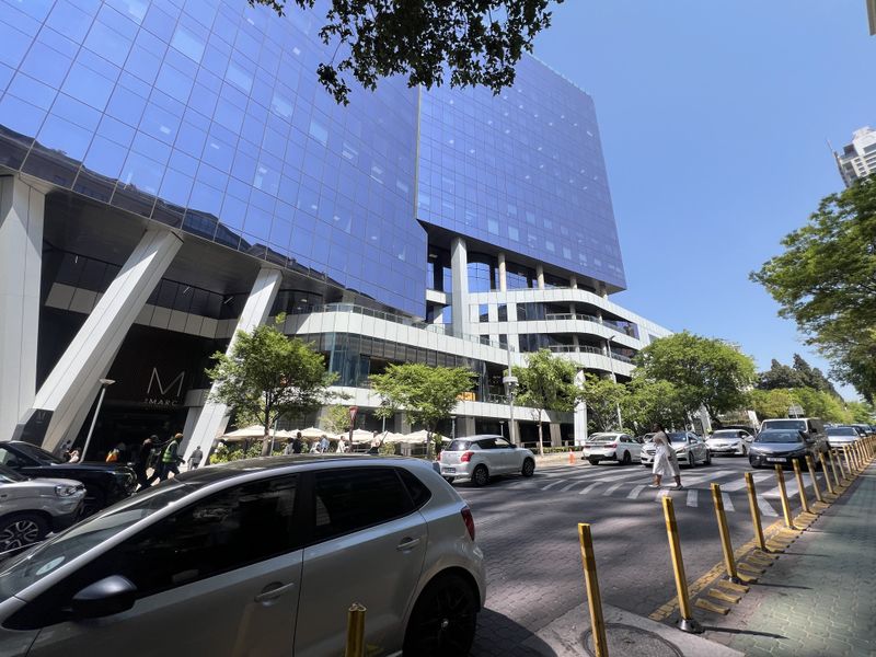 A modern commercial building featuring a prominent glass curtain wall facade and structural support columns, situated along a busy urban street.