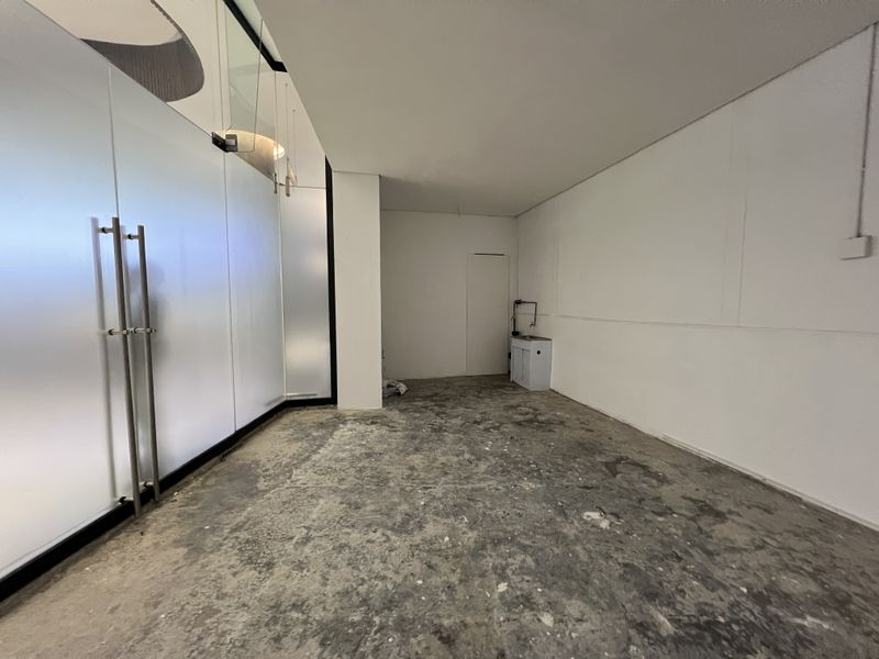 An empty utility or commercial space featuring a frosted glass partition, a small built-in sink unit, and unfinished concrete flooring.